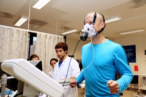 Man running on treadmill wih mask on, three persons are preforming a VO2 max test.